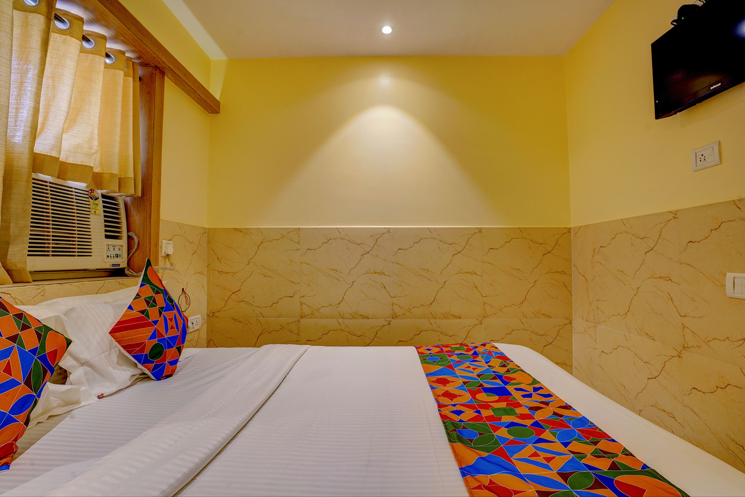 A hotel room with two beds, a ceiling fan, a mounted TV, and a window with curtains.