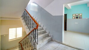 A staircase with marble steps and a wooden handrail, leading to a room with a light blue wall and framed pictures. - Fabhotel Luxury Stay (Bidhannagar)