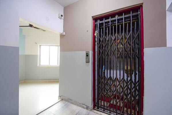A hallway with a metal gate, a ceiling fan, and a window. - Fabhotel Luxury Stay (Bidhannagar)