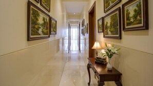 A hallway with framed landscape paintings on the walls, a polished marble floor, and a table with a lamp and books. - Fabexpress Super 7 Inn (Navi Mumbai)