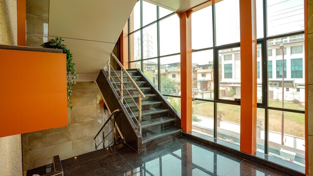 A modern interior with a glass staircase, large windows, and a view of the outside. - Fabexpress Super 7 Inn (Navi Mumbai)