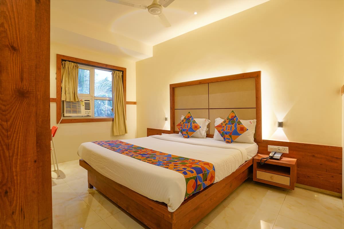 A bedroom with a wooden bed, a nightstand with a phone, a window with curtains, and a ceiling fan.