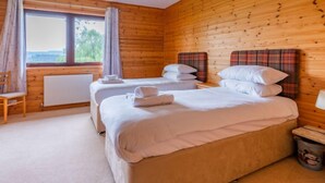 Ein Schlafzimmer einer Holzhütte mit zwei Betten, einem Fenster, einem Heizkörper und einem Holzstuhl.