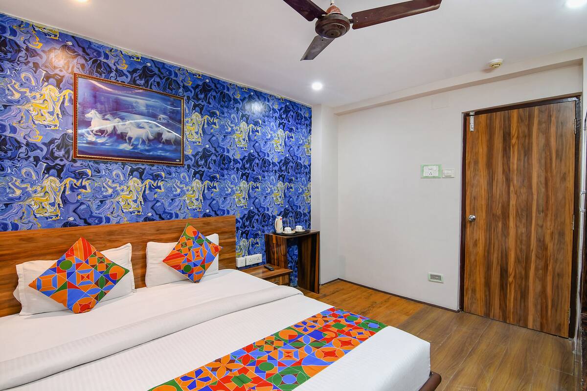 A hotel room with a bed, a ceiling fan, a wooden door, and a wall with a blue abstract pattern.