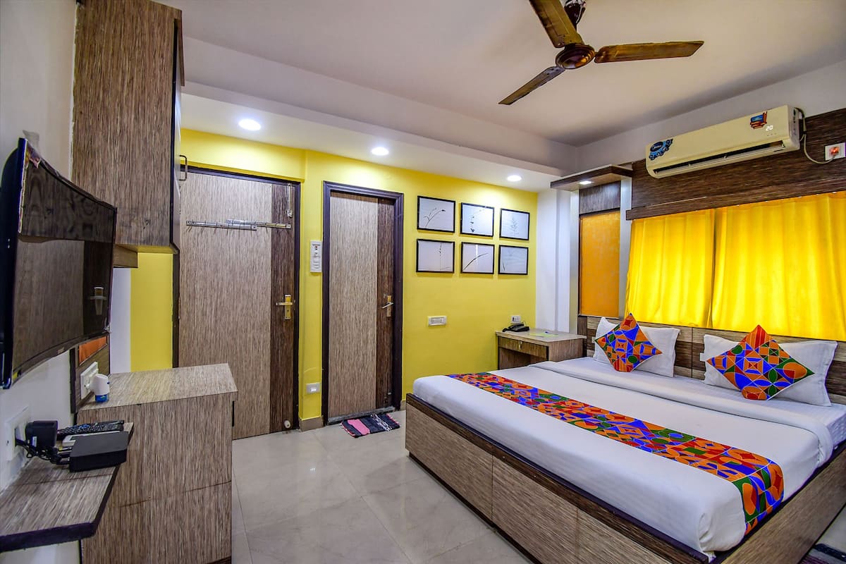 Habitación de hotel con cama, escritorio, silla, televisor y ventilador de techo.