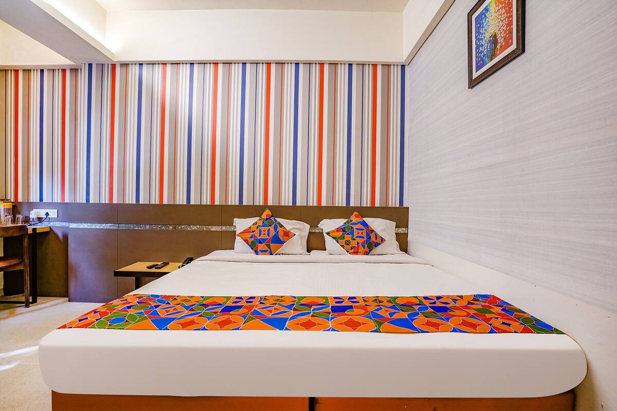 A hotel room with a striped wall, a bed with a colorful bedspread, and a framed picture on the wall.