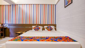 Une chambre d’hôtel avec un mur à rayures, un lit recouvert d’une courtepointe colorée et un tableau encadré accroché au mur.