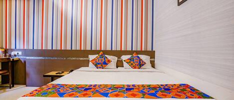 A hotel room with a striped wall, a bed with a colorful bedspread, and a framed picture on the wall.