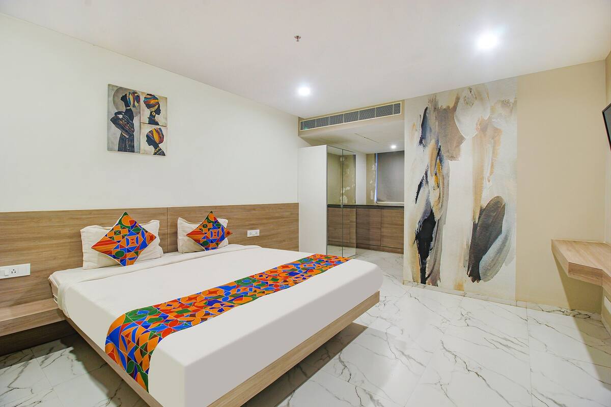 Habitación de hotel moderna con una cama grande, un cuadro en la pared y un baño visible a través de una puerta abierta.
