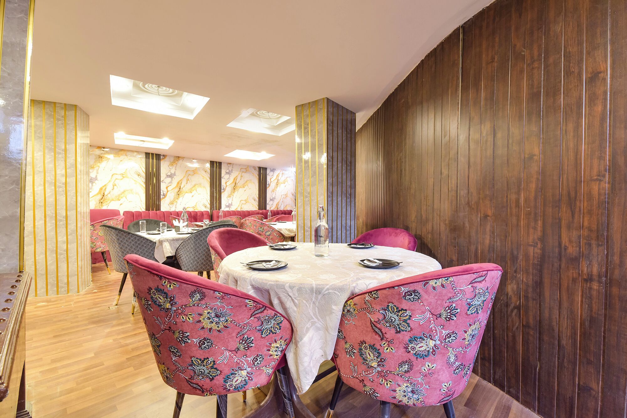A restaurant with a round table set for four, surrounded by pink upholstered chairs with floral patterns.