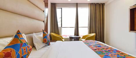 A hotel room with a large bed, two yellow chairs, a small table, and a window with curtains.
