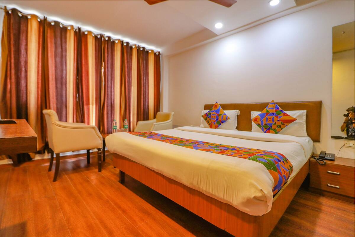 Habitació d'hotel amb sòl de fusta, un llit amb estovatge de colors, dos almoinos, una tauleta de nit, una cadira i un escriptori.