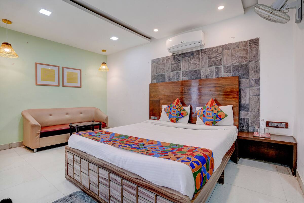 A hotel room with a bed, a sofa, a nightstand, and a wall-mounted air conditioner.