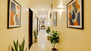 Corredor de hotel com arte abstrata emoldurada nas paredes, plantas em vasos e piso polido.
