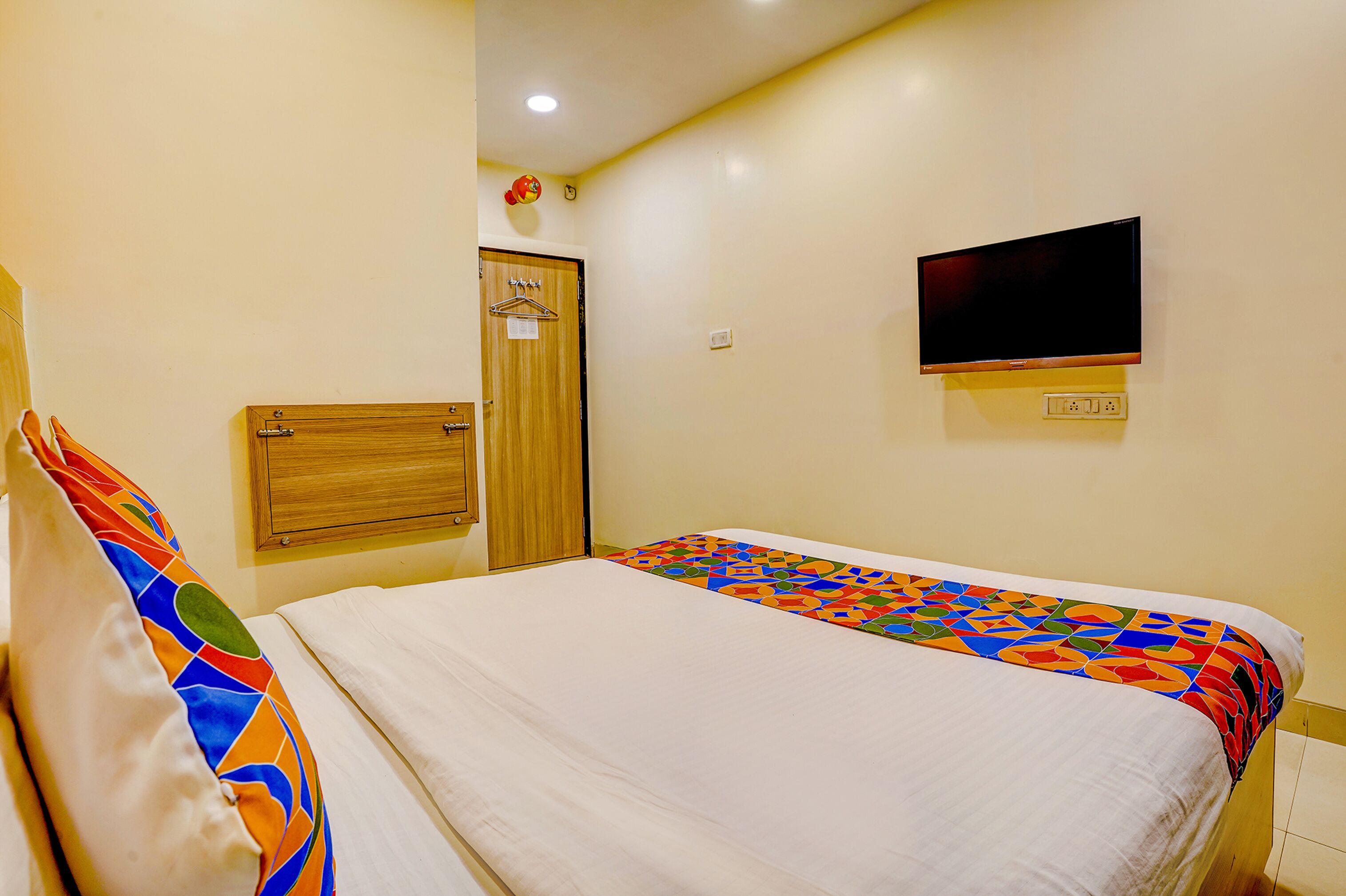 A hotel room with a bed, a TV mounted on the wall, and a wooden door.