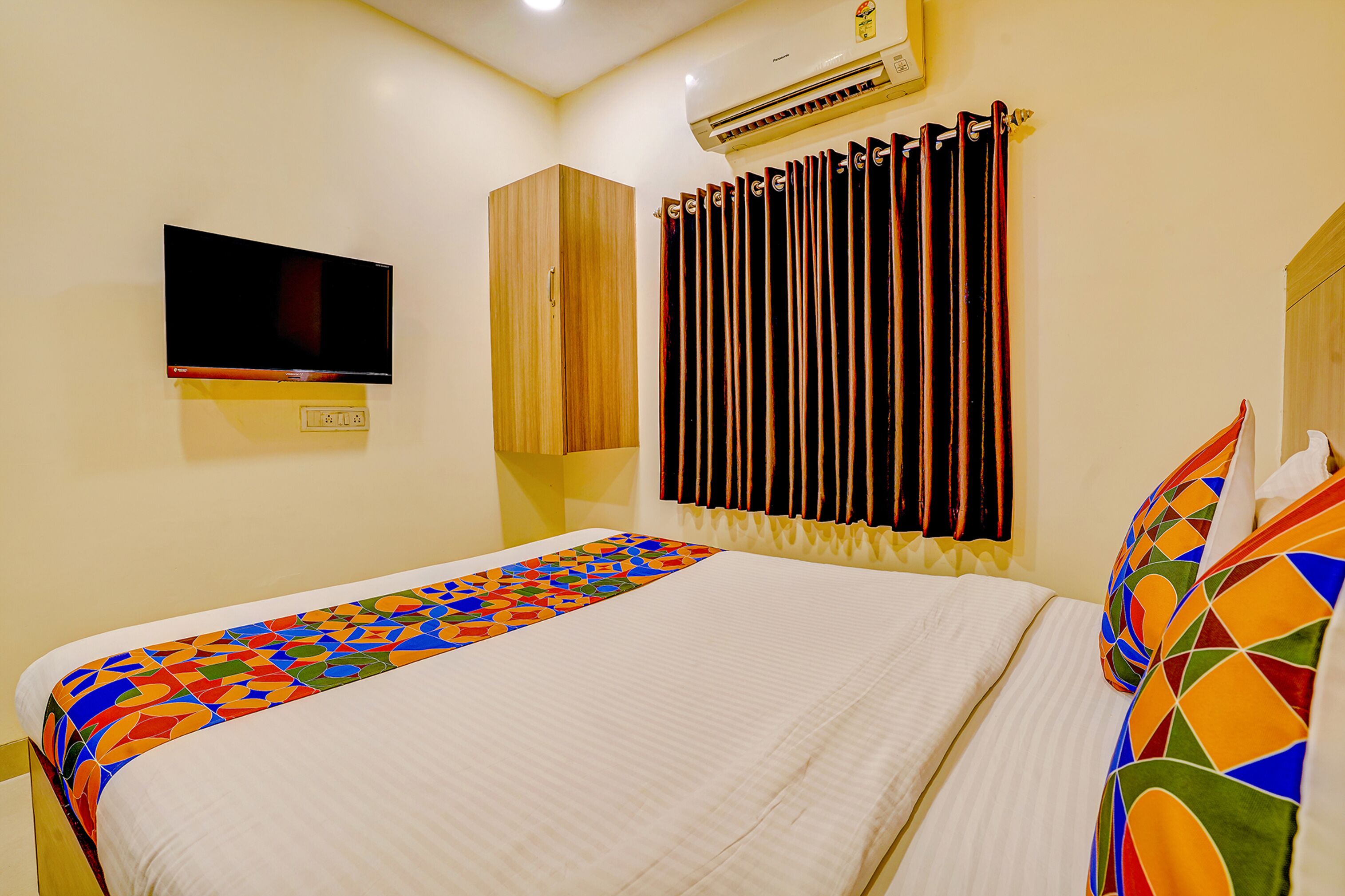 Une chambre d’hôtel équipée d’un lit, d’un téléviseur fixé au mur, d’un climatiseur et d’une fenêtre avec des rideaux.