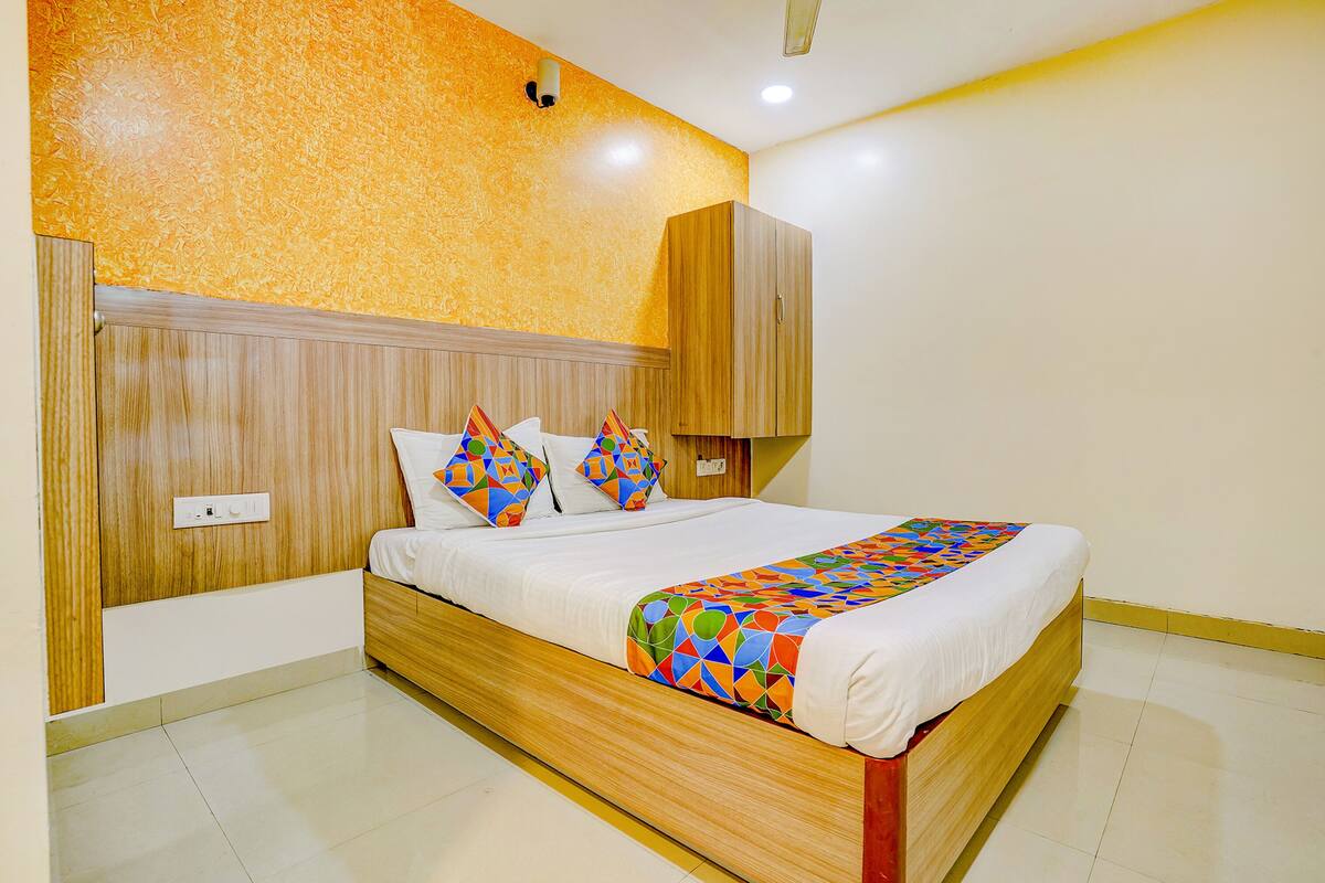 Un dormitorio con estructura de cama de madera, ropa de cama blanca y un plaid de estampado geométrico colorido.