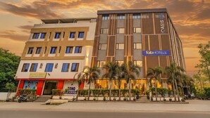 A modern hotel with a prominent 'fabHOTELS' sign, featuring a multi-story structure with a mix of glass and wooden paneling, and a well-maintained outdoor area with palm trees.