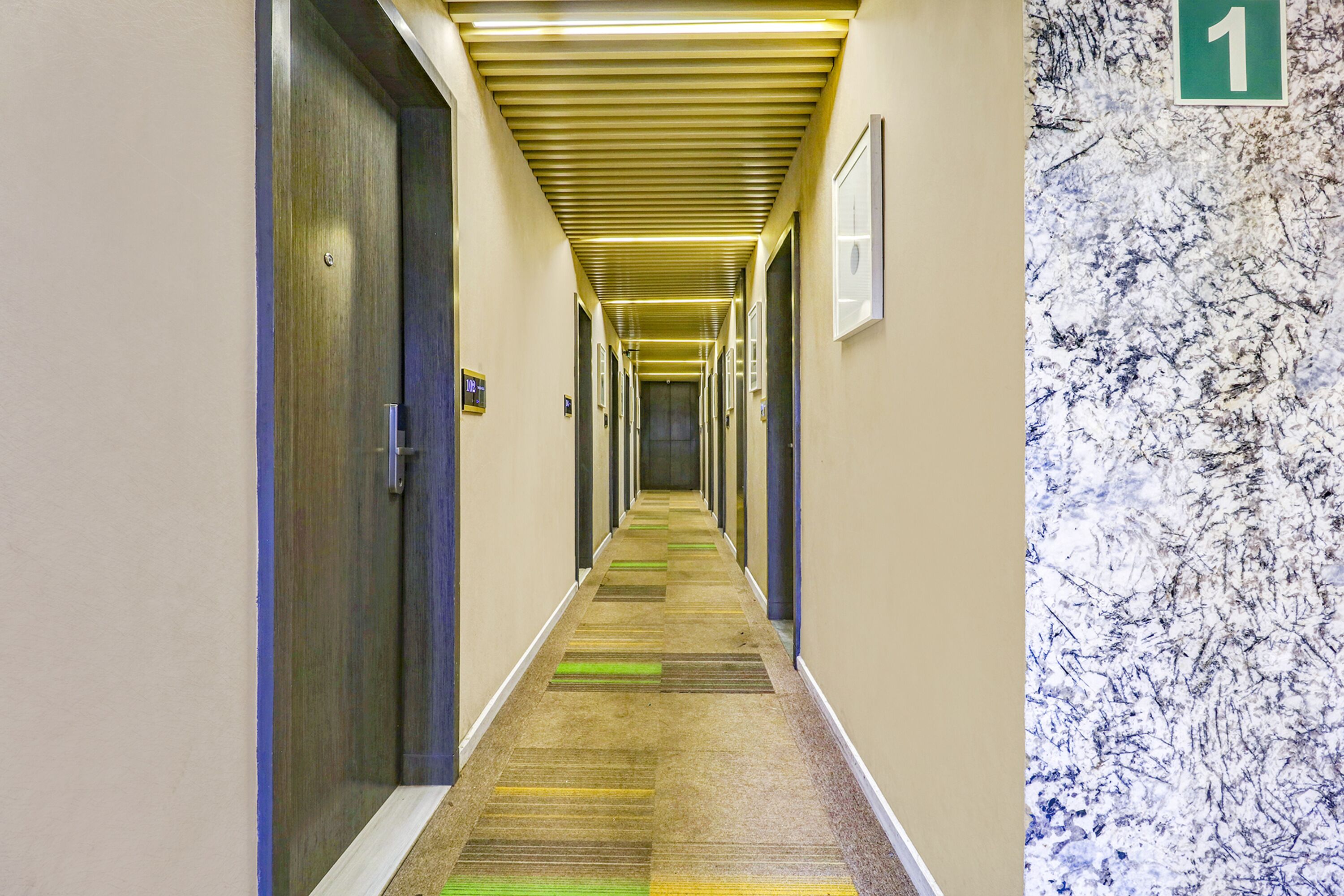 A long, narrow hallway with doors on both sides, a carpeted floor, and a number sign indicating room 1.