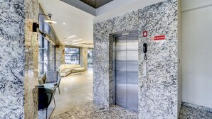 A modern elevator with a marble wall, a "No Smoking" sign, and a seating area with a sofa and chairs.
