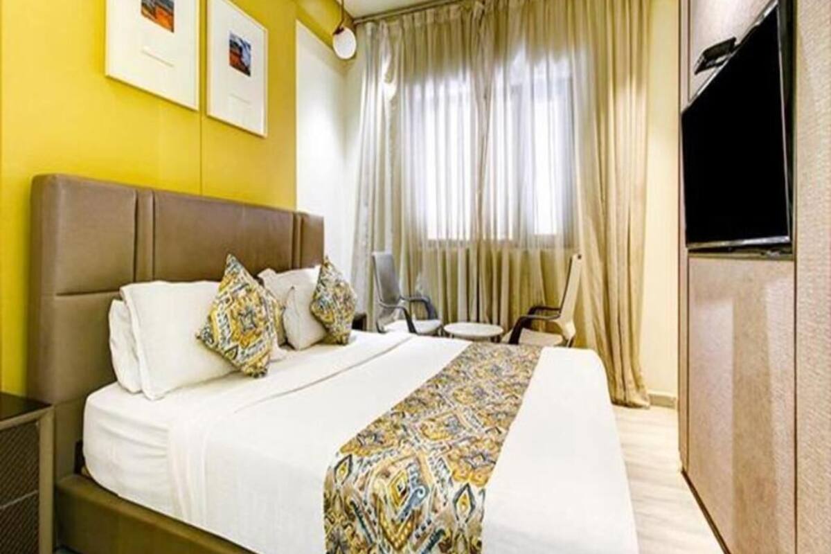 Quarto de hotel com cama, escrivaninha, cadeira, televisão e cortinas.