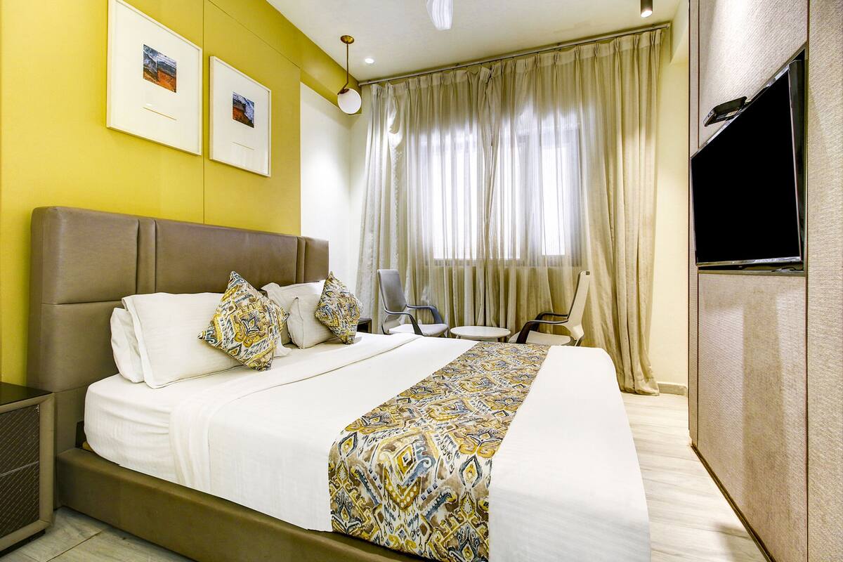 Quarto de hotel com uma cama grande, televisão de tela plana, escrivaninha e uma cadeira.