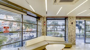 A modern lobby with a beige sofa, a white table, and large windows offering views of the street and palm trees.