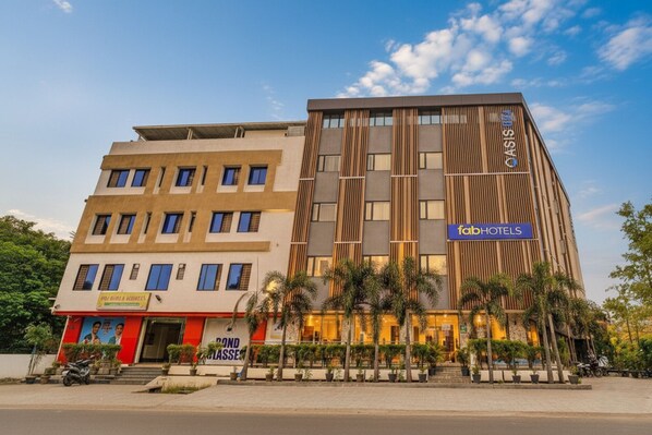Un hotel moderno con un llamativo letrero de 'FabHotels', varios pisos y un área exterior bien cuidada con plantas en macetas.