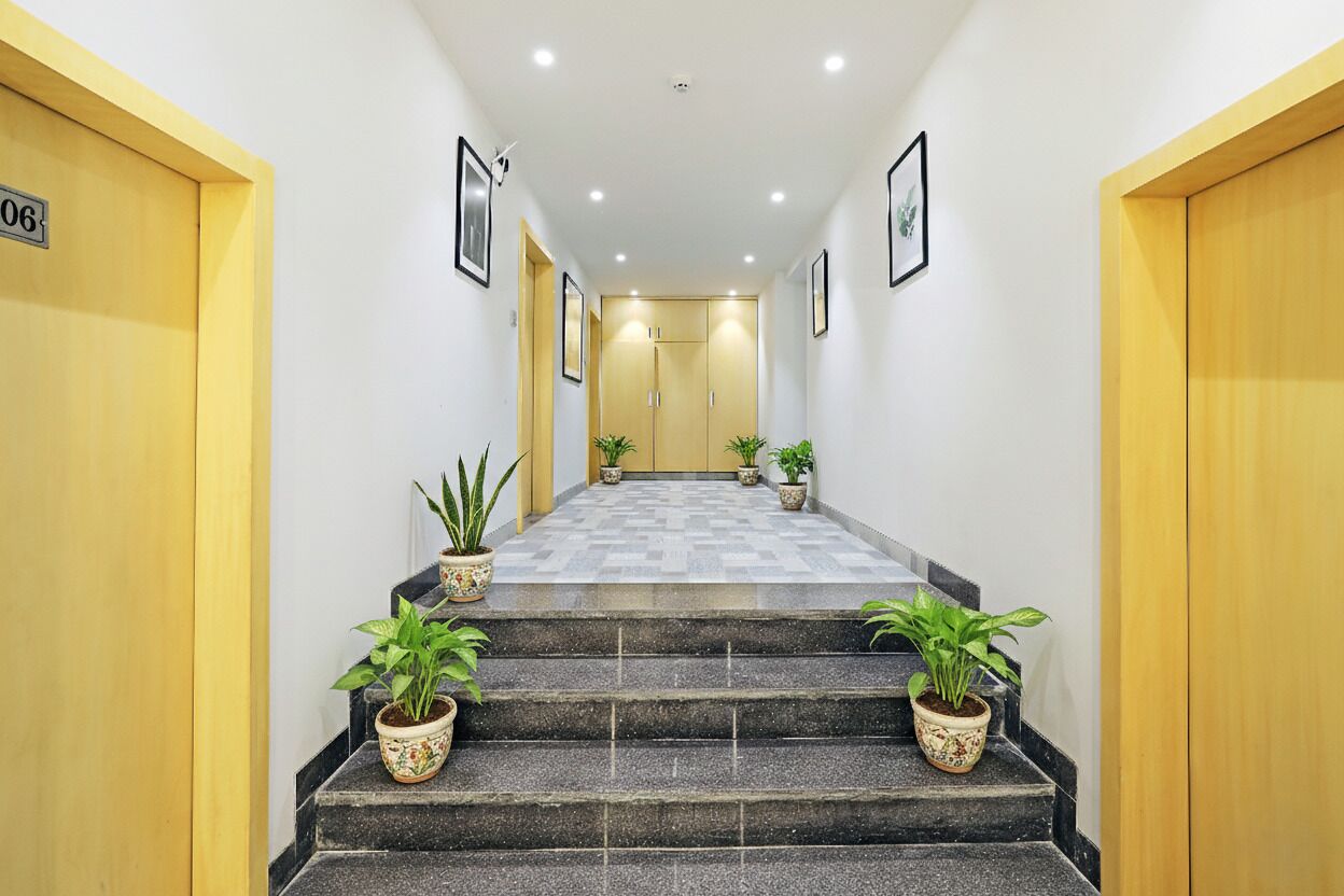A hotel hallway with a staircase, potted plants, and doors marked with room numbers.