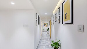 A hallway with framed artwork on the walls, a patterned floor, and a potted plant. - FabHotel Yellow Courtyard (Bhopal)