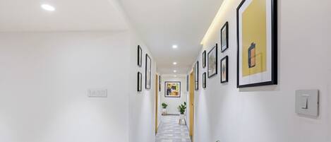 A hallway with framed artwork on the walls, a patterned floor, and a potted plant.