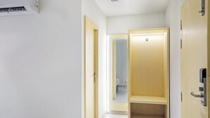 A narrow hallway with a white wall, a wooden door, and a mirror reflecting a bathroom. - FabHotel Yellow Courtyard (Bhopal)