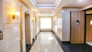 A hotel corridor with marble flooring, wall-mounted lighting, and a large window at the end. - FabHotel Sapphire 83 Best hotel in Manesar, Gurugram (Gurugram)