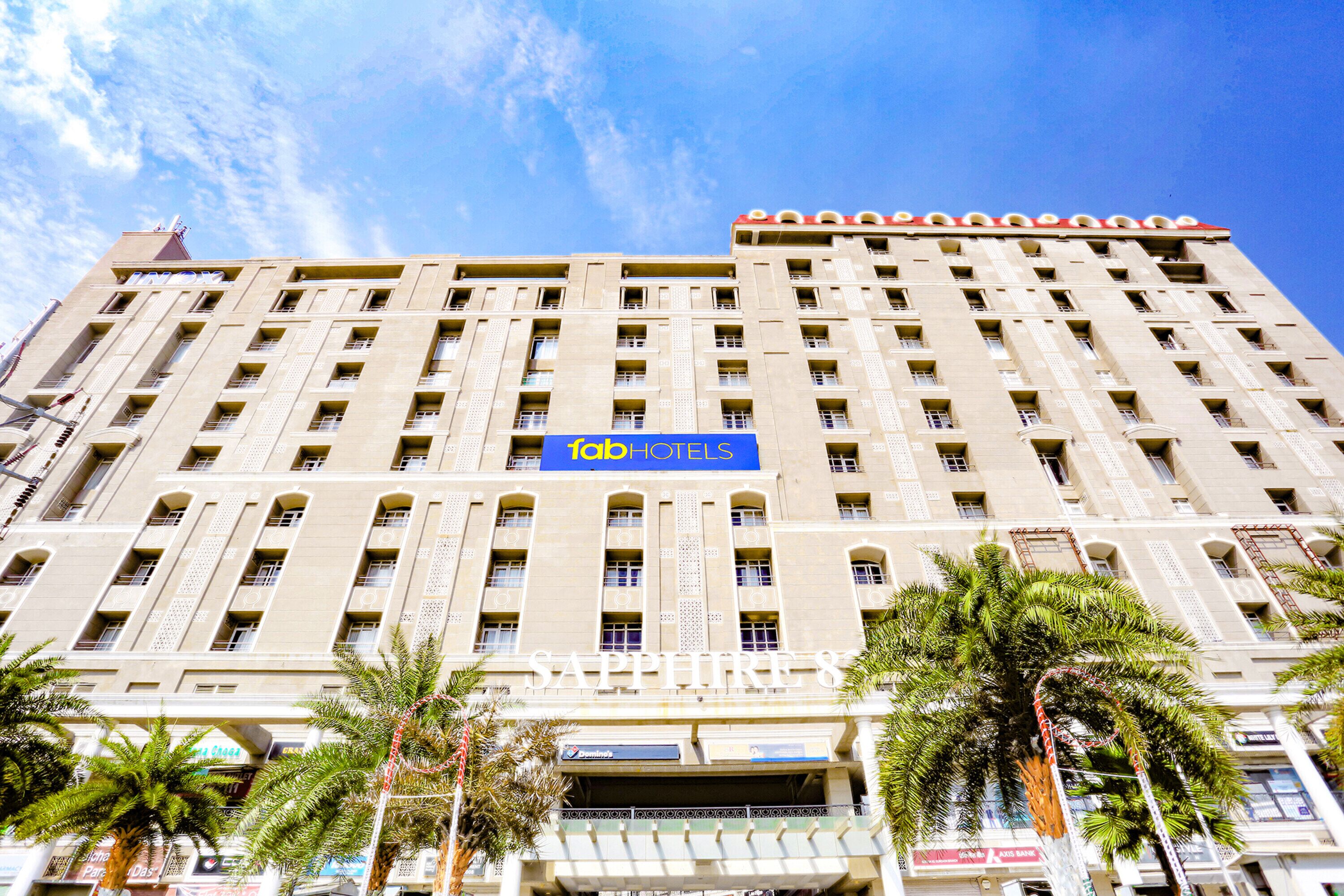 Een hoog hotelgebouw met een opvallend 'FabHotels'-bord, meerdere balkons en palmbomen ervoor.