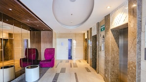 A modern lobby with a marble floor, a reception desk, a seating area with a purple chair, and an elevator. - FabHotel Sapphire 83 Best hotel in Manesar, Gurugram (Gurugram)