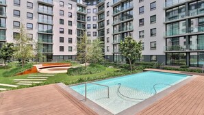 A modern apartment complex with a swimming pool, green spaces, and a wooden deck.