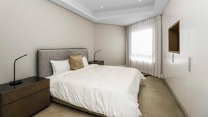 A modern hotel room with a large bed, a nightstand, a desk, and a window with curtains.