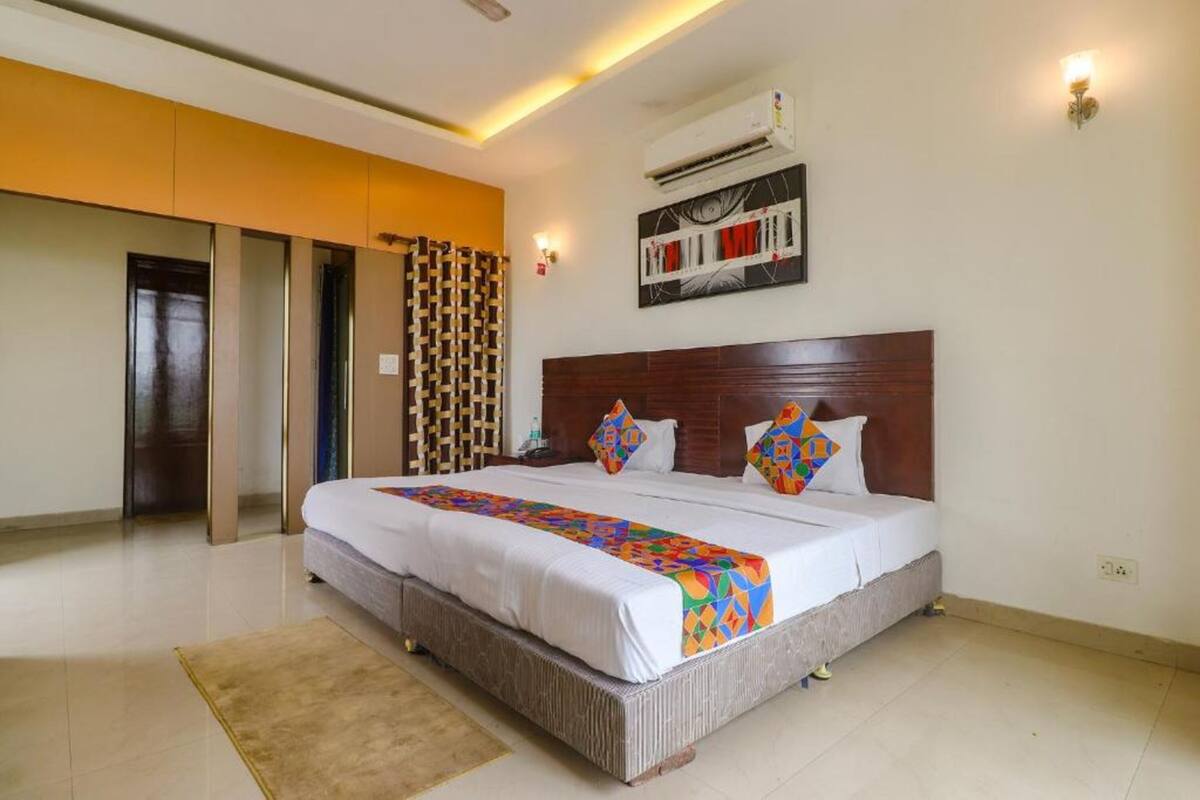 Une chambre d’hôtel avec un grand lit, une tête de lit en bois, un rideau à motifs et un climatiseur fixé au mur.