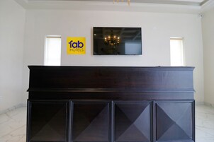 Un mostrador de recepción de madera oscura con un televisor de pantalla plana encima. Hay un letrero de 'Tab Hotels' en la pared.