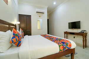 Uma cama bem arrumada com almofadas coloridas, cabeceira de madeira, mesa de cabeceira, televisão e ar condicionado.
