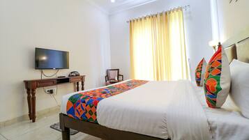 A hotel room with a bed, a desk with a television, a chair, and a window with curtains.
