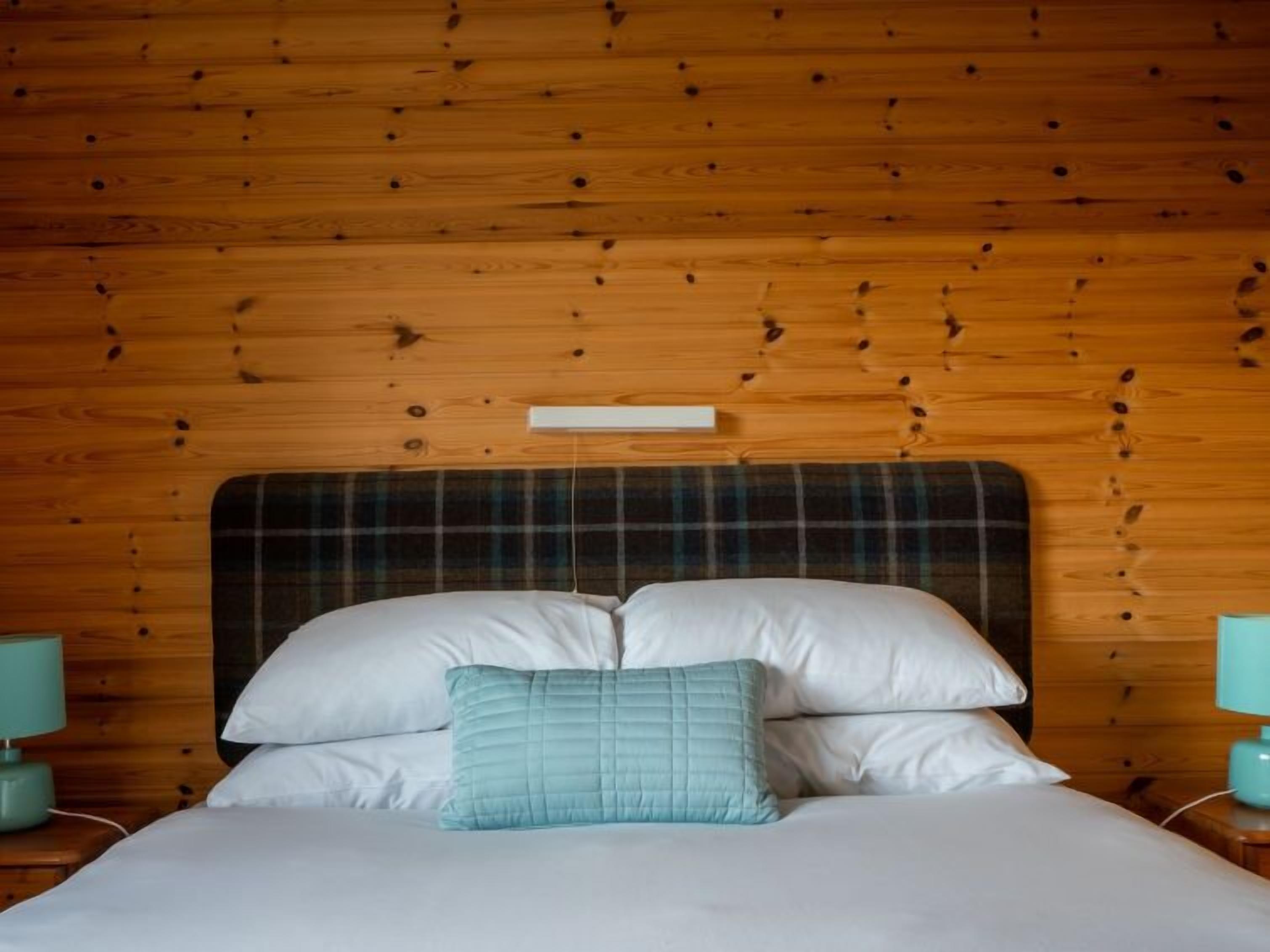 A bed with a plaid headboard, white pillows, and a teal accent pillow.