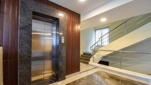 An elevator with a granite panel, a wooden wall, and a staircase with metal railings. - Fabhotel Gargi Inn (Pune)
