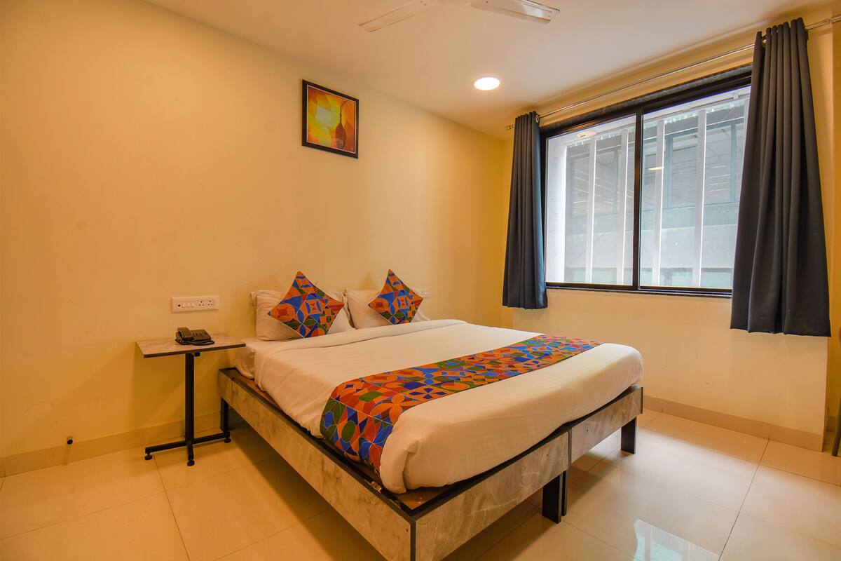 Habitación de hotel con cama, mesita de noche con teléfono, ventana con cortinas y un cuadro en la pared.