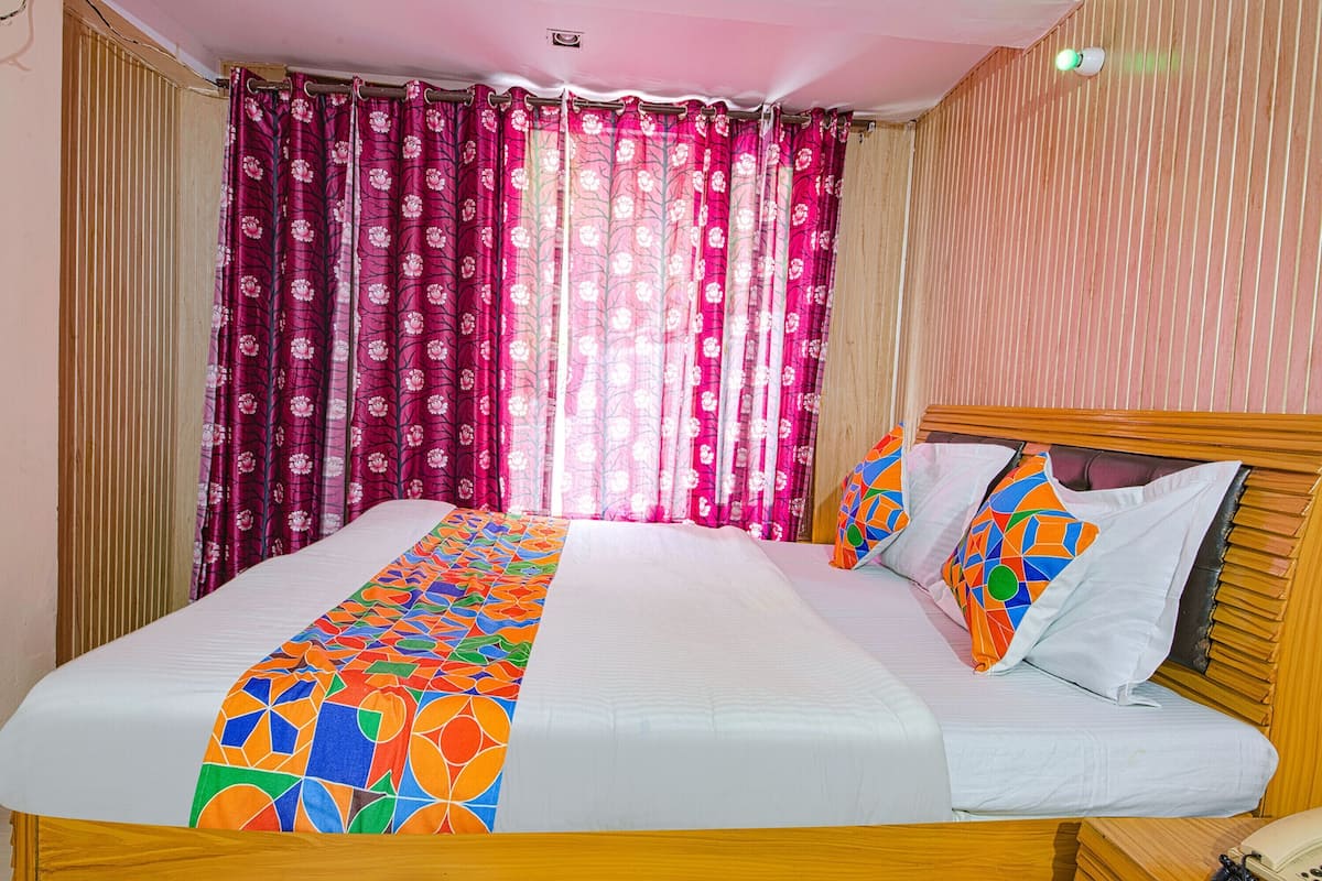 Una cama con un edredón de estampado geométrico y colorido, un cabecero de madera y una cortina con diseño floral.
