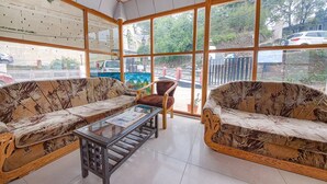 A room with two sofas, a small table, and large windows offering a view of the street and parked cars. - FabHotel Sapphire (Dehradun)