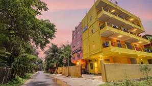 A multi-story yellow building with balconies, a gated entrance, and a street lined with trees. - Fabhotel Knight Airways (Guwahati)