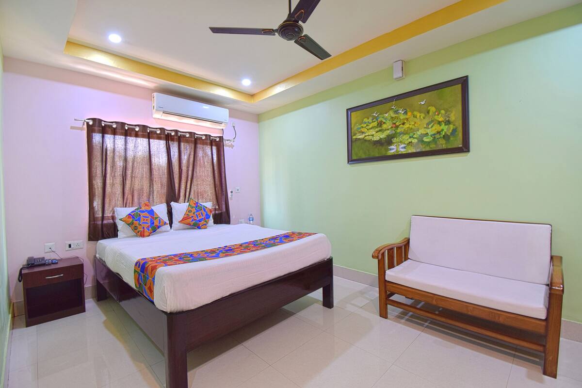 A bedroom with a bed, a wooden bench, an air conditioning unit, and a painting on the wall.