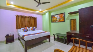 A neatly arranged bedroom with a bed, bedside table, a desk, a chair, a ceiling fan, and a painting on the wall. - Fabhotel Knight Airways (Guwahati)