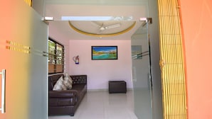 A modern living room with a brown leather sofa, a glass partition, and a ceiling fan. - Fabhotel Knight Airways (Guwahati)